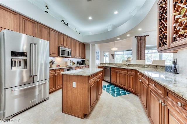 kitchen with appliances with stainless steel finishes, a sink, light stone countertops, and brown cabinets