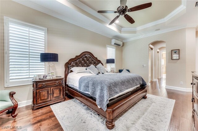 bedroom featuring arched walkways, a raised ceiling, hardwood / wood-style floors, and a wall mounted air conditioner