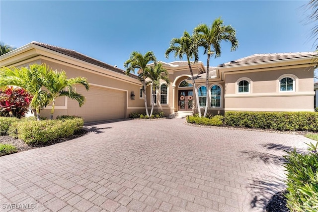 mediterranean / spanish home with decorative driveway, french doors, a tile roof, stucco siding, and an attached garage