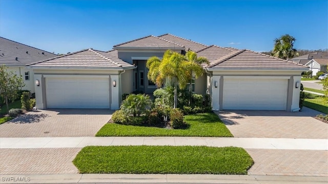 single story home featuring stucco siding, a tiled roof, decorative driveway, and a garage