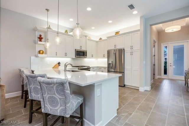 kitchen featuring visible vents, a kitchen bar, a peninsula, stainless steel appliances, and a sink