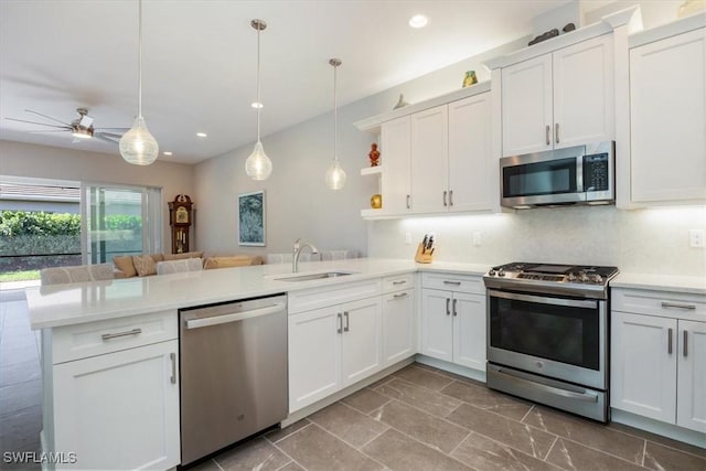 kitchen with a sink, open shelves, appliances with stainless steel finishes, a peninsula, and light countertops