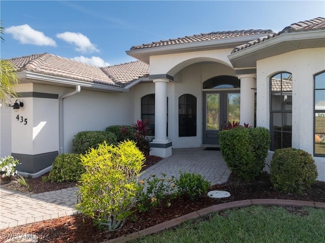 view of exterior entry featuring an attached garage, a tile roof, and stucco siding