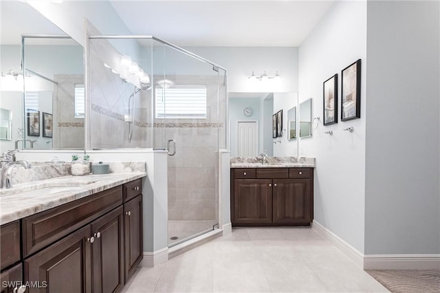 full bath with a stall shower, two vanities, a sink, and baseboards