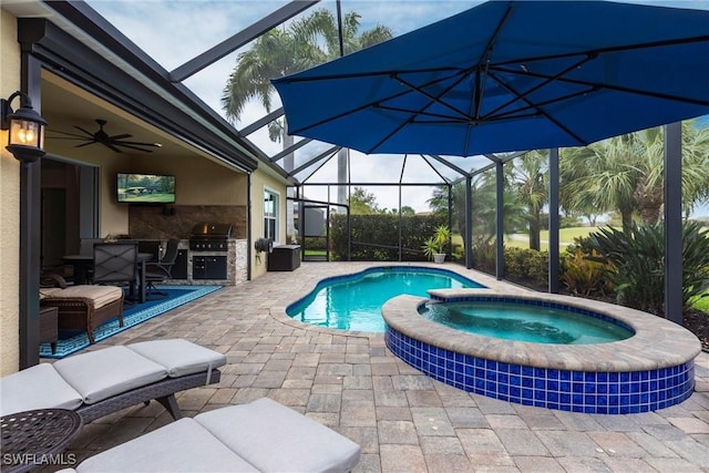 view of pool with a patio, a pool with connected hot tub, glass enclosure, ceiling fan, and exterior kitchen