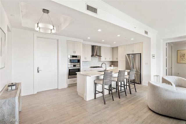 kitchen featuring wall chimney range hood, visible vents, stainless steel appliances, a kitchen breakfast bar, and light wood-type flooring