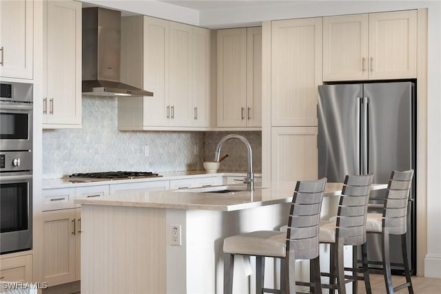 kitchen with stainless steel appliances, a sink, a kitchen bar, wall chimney range hood, and backsplash