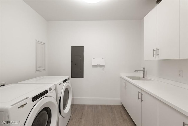 washroom with electric panel, cabinet space, a sink, light wood-style floors, and washer and dryer