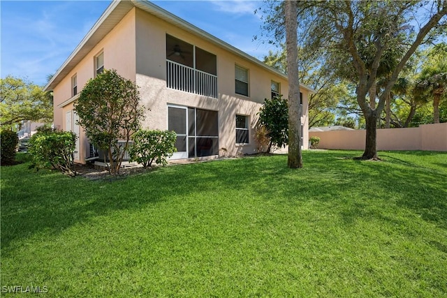 rear view of house with ceiling fan, a yard, fence, and stucco siding