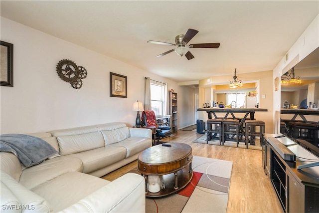 living room with light wood-style flooring and ceiling fan with notable chandelier