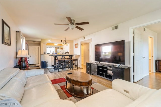 living area featuring a ceiling fan, wood finished floors, visible vents, and baseboards