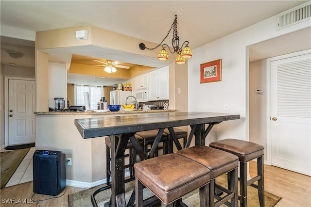 dining space featuring light wood-type flooring, visible vents, a raised ceiling, ceiling fan with notable chandelier, and baseboards