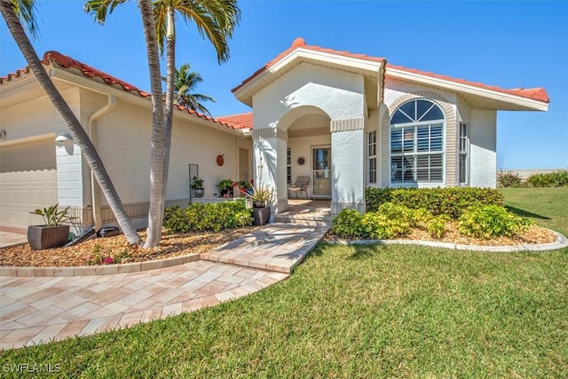 mediterranean / spanish house featuring a garage, a tile roof, a front yard, and stucco siding