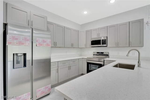 kitchen featuring appliances with stainless steel finishes, gray cabinets, a sink, and light stone counters