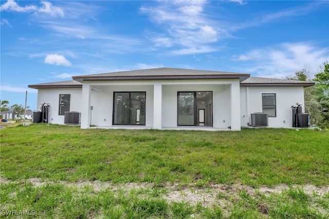 rear view of house with central AC, a lawn, and stucco siding