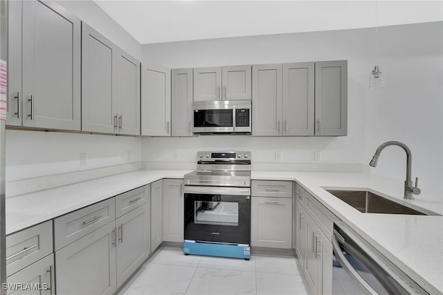 kitchen with light stone counters, appliances with stainless steel finishes, marble finish floor, gray cabinets, and a sink