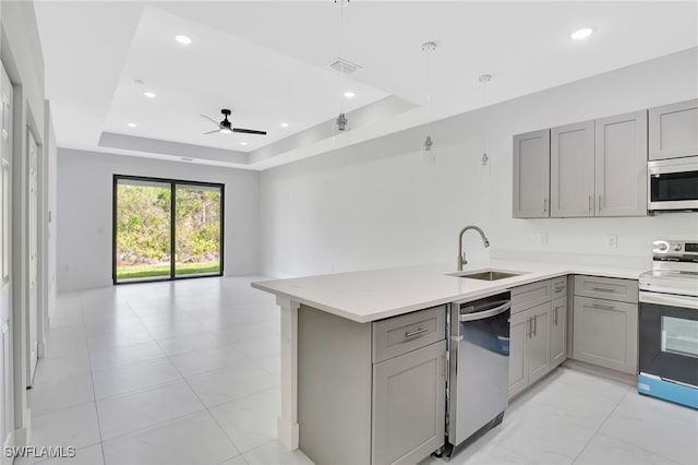 kitchen with a raised ceiling, stainless steel appliances, a sink, and gray cabinetry