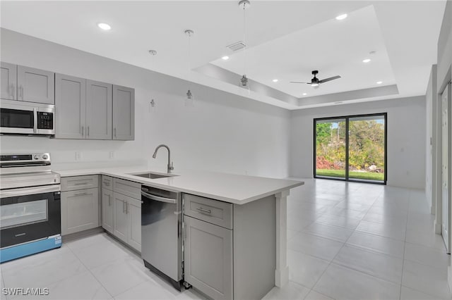 kitchen featuring gray cabinets, a tray ceiling, stainless steel appliances, and a sink