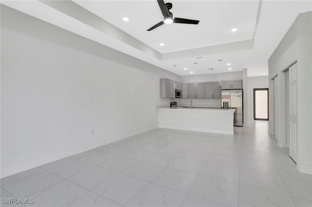 unfurnished living room featuring a ceiling fan, recessed lighting, a raised ceiling, and baseboards