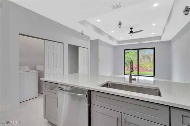 kitchen with washer and clothes dryer, dishwasher, a tray ceiling, gray cabinetry, and a sink