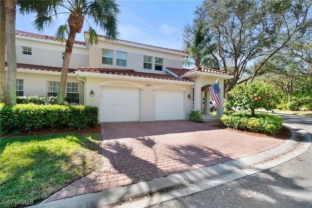 mediterranean / spanish-style home with a garage, decorative driveway, a tile roof, and stucco siding