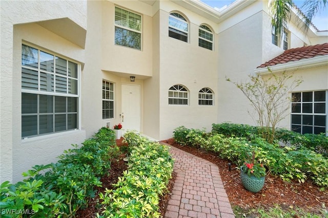 entrance to property featuring a tiled roof and stucco siding