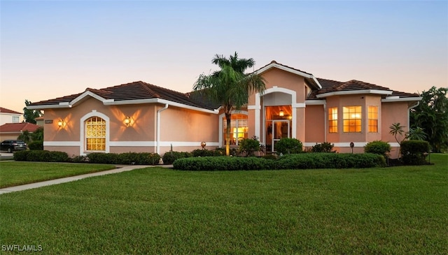 mediterranean / spanish home with a front lawn, a tile roof, and stucco siding