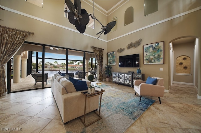 living area featuring baseboards, arched walkways, ceiling fan, tile patterned floors, and crown molding