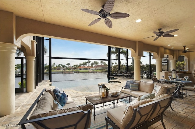 view of patio / terrace featuring a water view, a lanai, an outdoor living space, and a ceiling fan