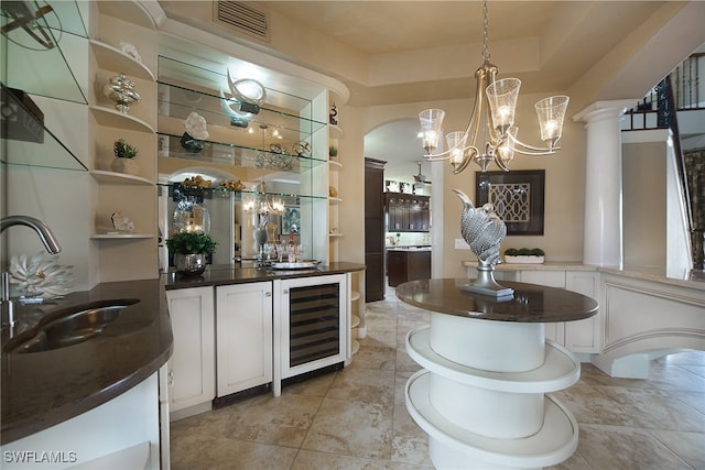 bar with beverage cooler, a sink, hanging light fixtures, wet bar, and decorative columns