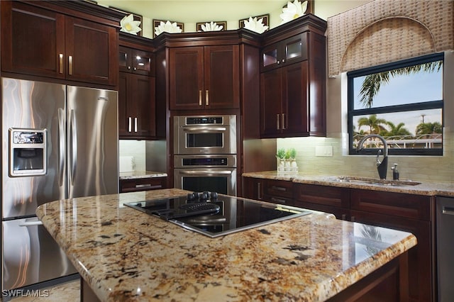 kitchen featuring decorative backsplash, appliances with stainless steel finishes, a center island, light stone countertops, and a sink