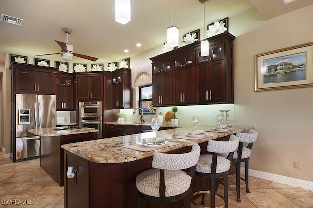 kitchen featuring light stone counters, stainless steel appliances, a peninsula, visible vents, and decorative backsplash