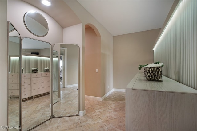 corridor featuring arched walkways, light tile patterned flooring, and baseboards