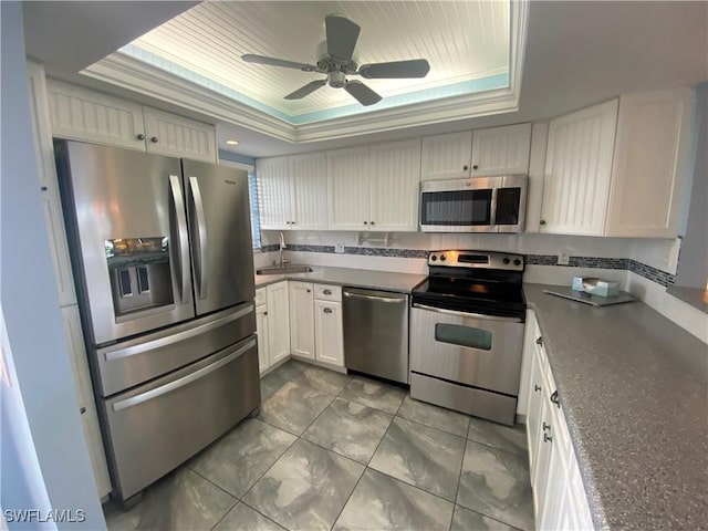 kitchen with crown molding, stainless steel appliances, a raised ceiling, white cabinets, and a sink