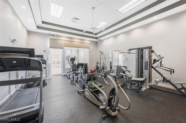 workout area featuring visible vents, a ceiling fan, a raised ceiling, and baseboards