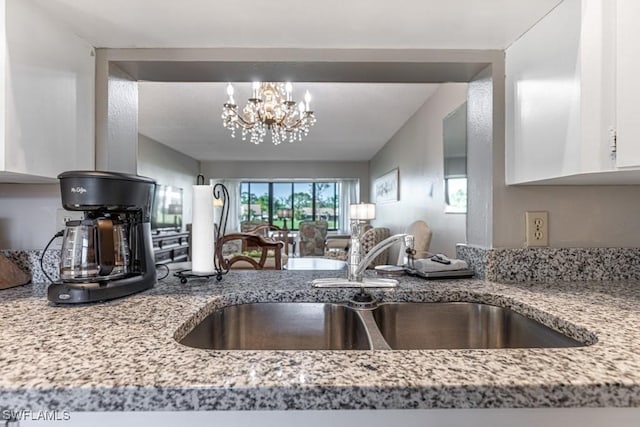 kitchen featuring a chandelier, white cabinetry, a sink, and light stone countertops