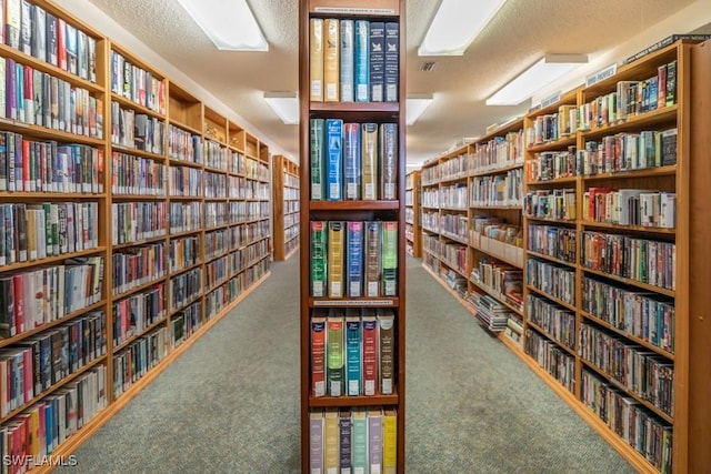 living area featuring wall of books, carpet, and a textured ceiling