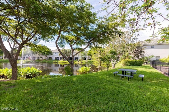 view of community featuring a lawn, fence, and a water view