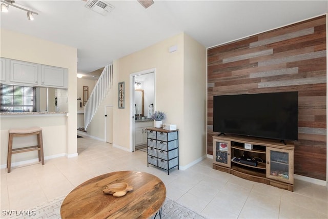 living area featuring visible vents, baseboards, stairway, wood walls, and light tile patterned flooring