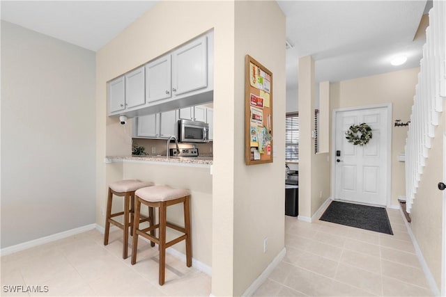 interior space with light tile patterned floors, baseboards, a breakfast bar, gray cabinets, and stainless steel microwave