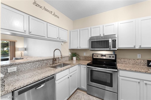 kitchen featuring a sink, a textured ceiling, appliances with stainless steel finishes, white cabinets, and light stone countertops