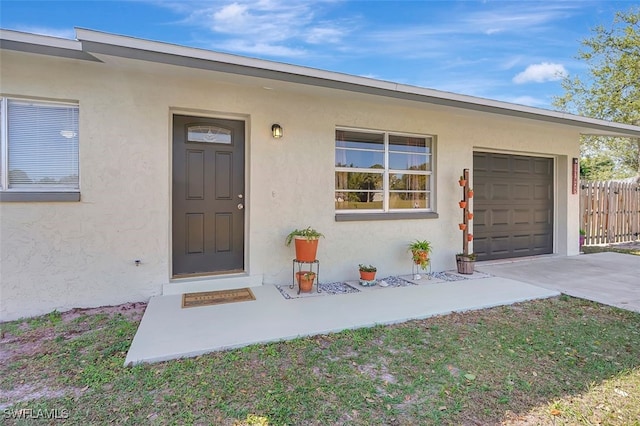 property entrance with a garage, driveway, fence, and stucco siding