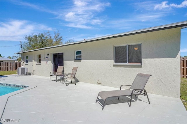 rear view of property featuring a fenced in pool, stucco siding, a patio area, central AC, and fence