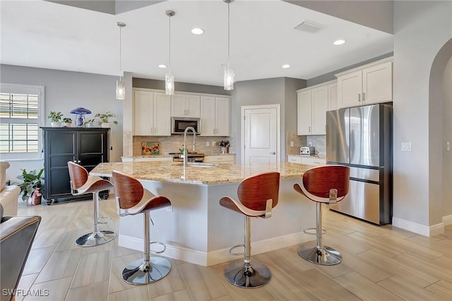 kitchen with a breakfast bar, light stone counters, white cabinetry, visible vents, and stainless steel appliances