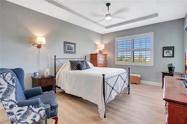 bedroom featuring a tray ceiling, baseboards, and light wood finished floors