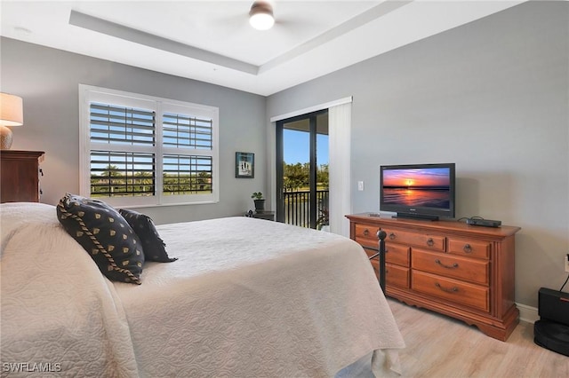 bedroom featuring a tray ceiling, access to exterior, baseboards, and wood finished floors