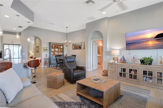 living room with light wood-style flooring, arched walkways, ceiling fan with notable chandelier, and visible vents