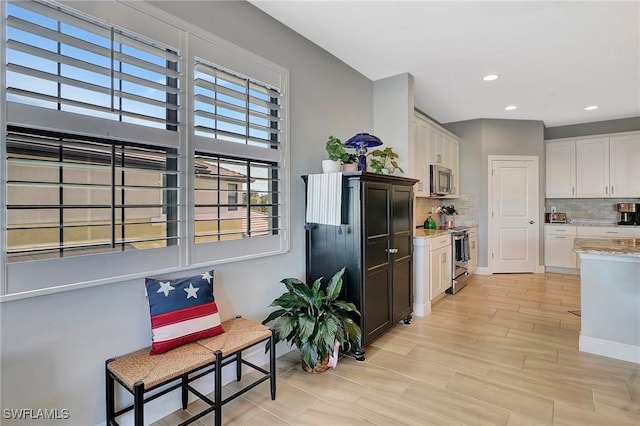 kitchen featuring tasteful backsplash, light stone counters, white cabinets, and stainless steel appliances
