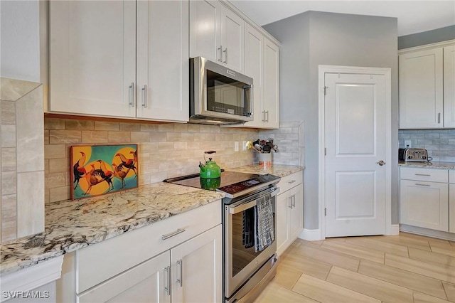 kitchen with tasteful backsplash, appliances with stainless steel finishes, white cabinetry, and light stone countertops