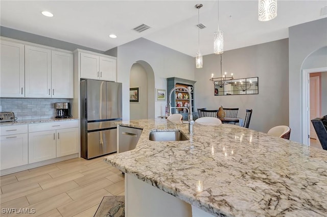kitchen with white cabinets, visible vents, decorative backsplash, stainless steel appliances, and arched walkways